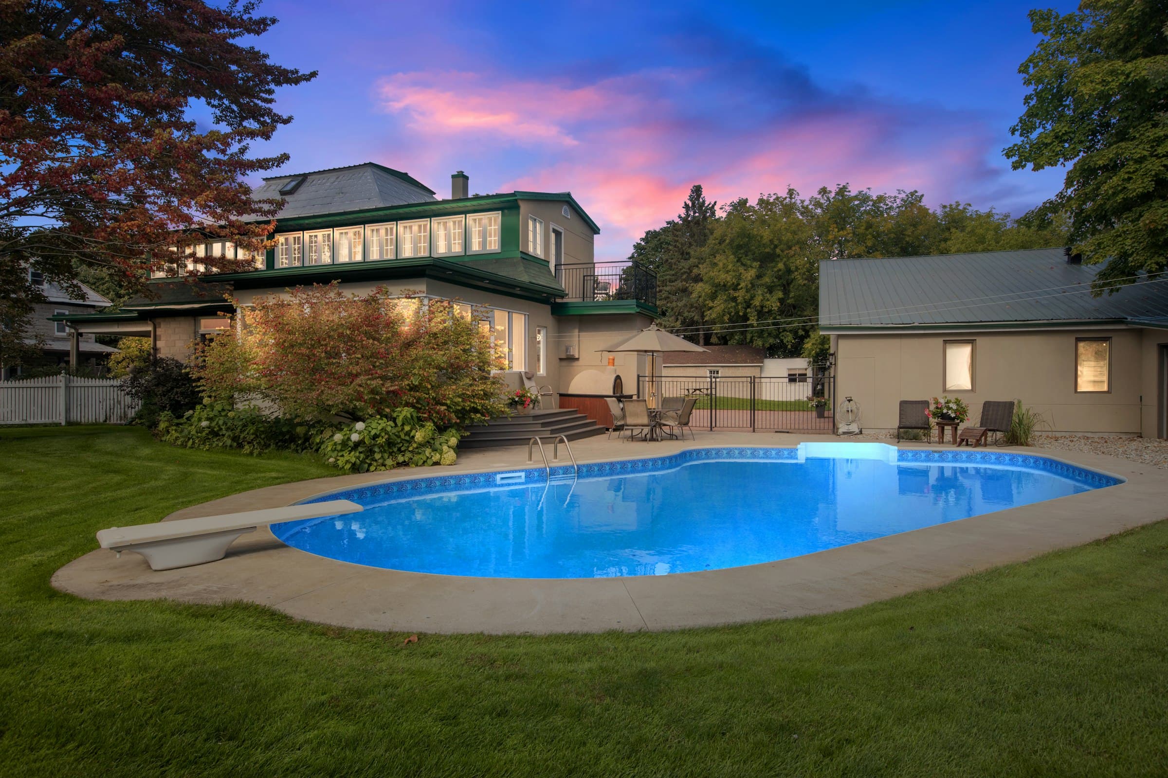 A backyard pool glowing blue at dusk on a lawn behind the house.
