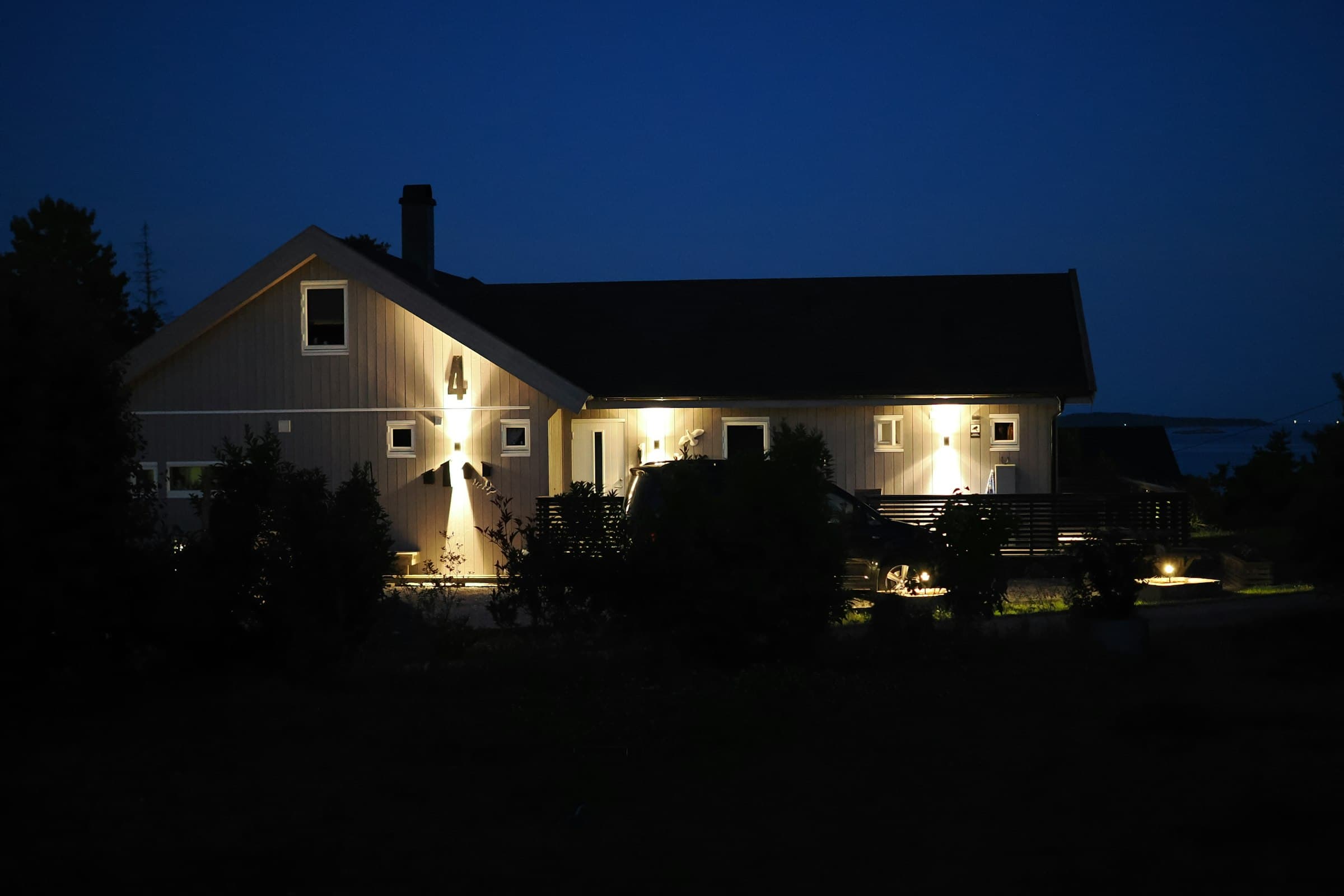A house at night with wall lights and planting lit along the front.