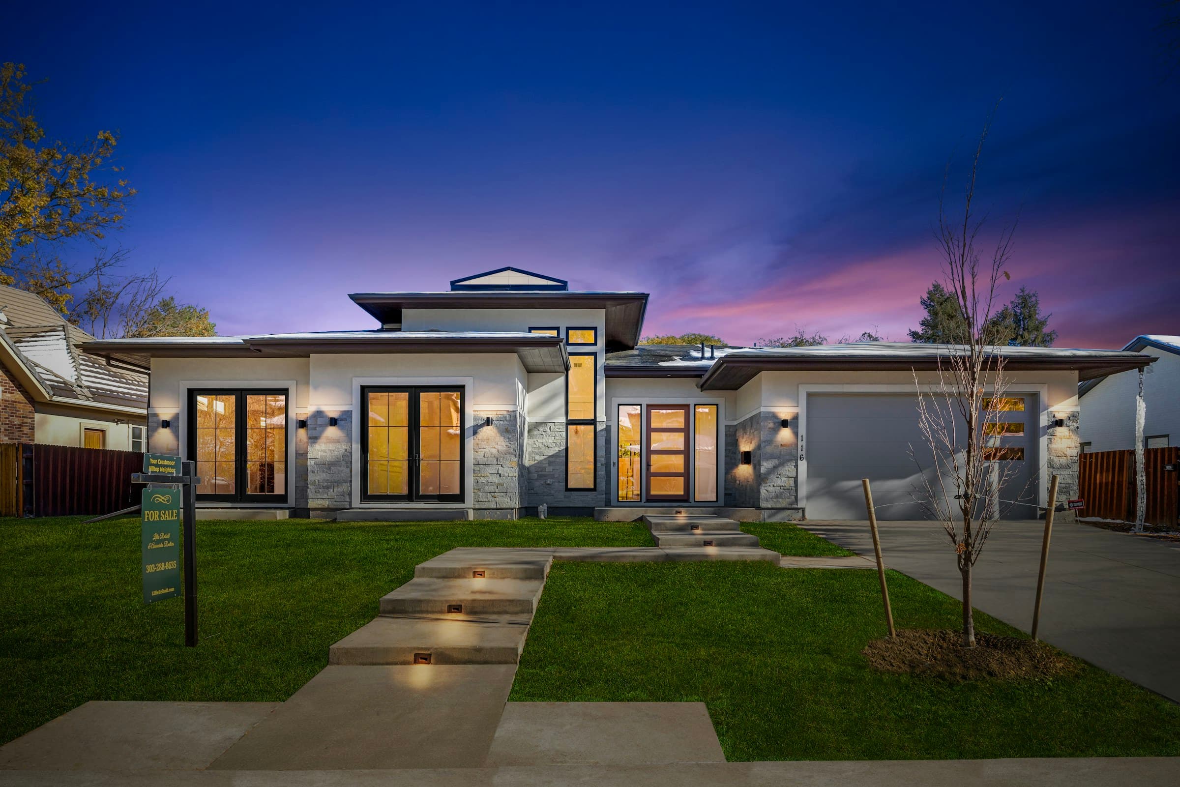A modern home at blue hour with lit steps along the front walkway and lawn.