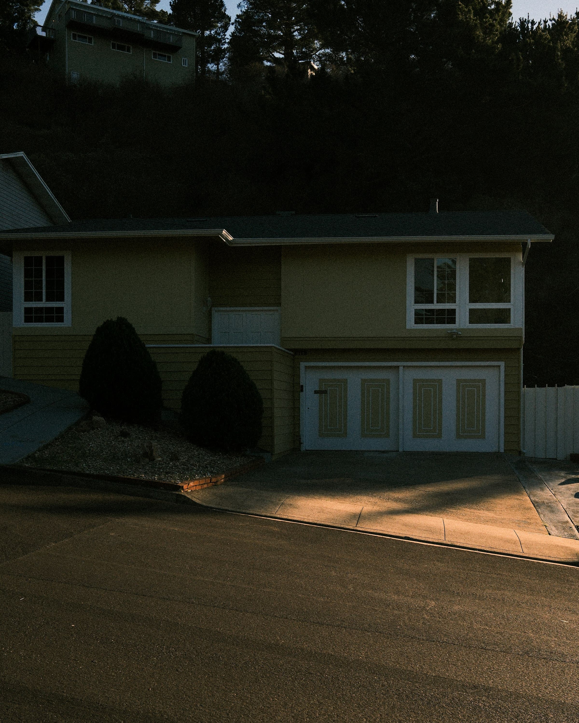 A split-level home at dusk, the front entry and shrubs lit warm.