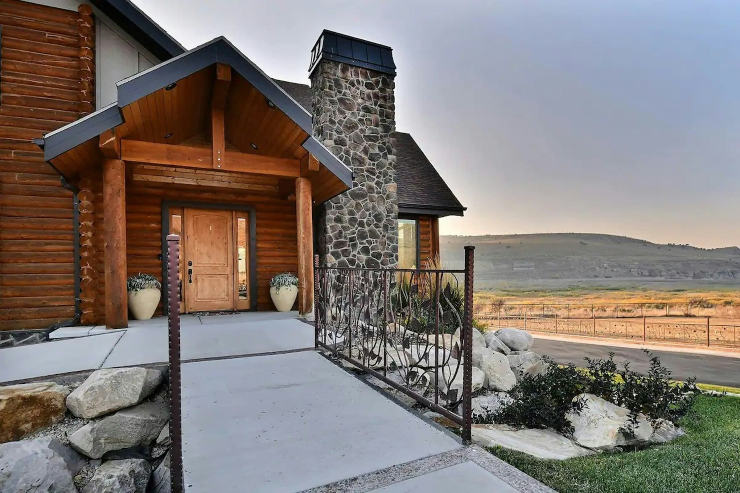 A timber and stone home entry with a stone chimney, boulders and planting along the walk.