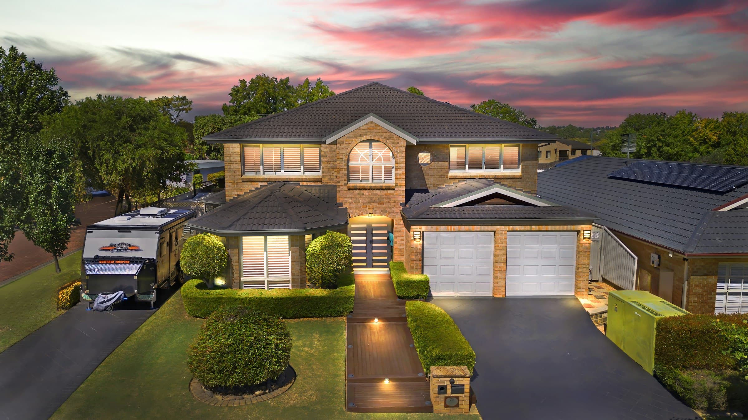 A large two-storey home at sunset, path lights leading up the front walk.